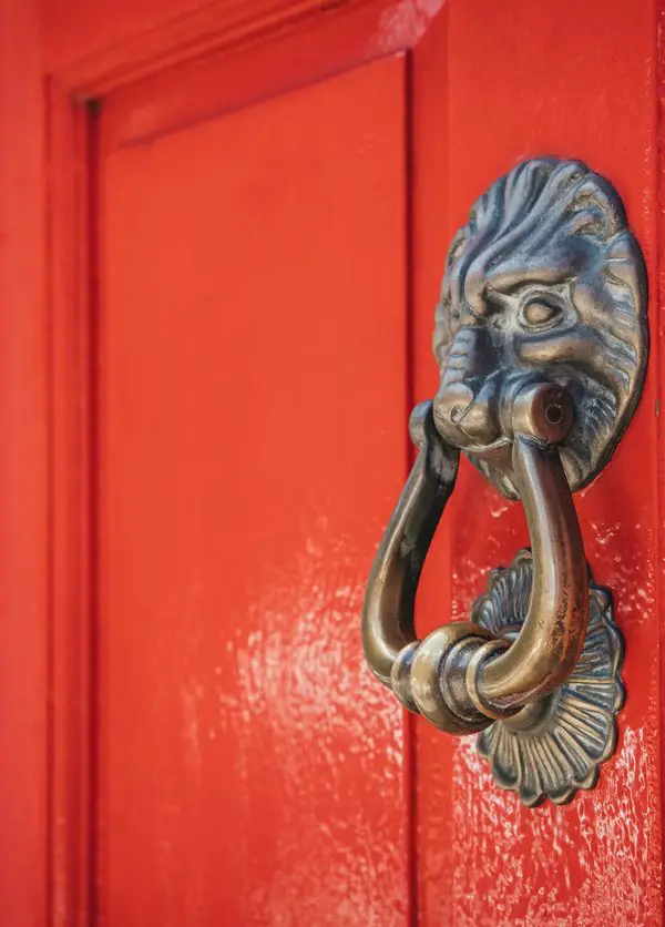 Close up of a lion's head door knocker on a bright red door.